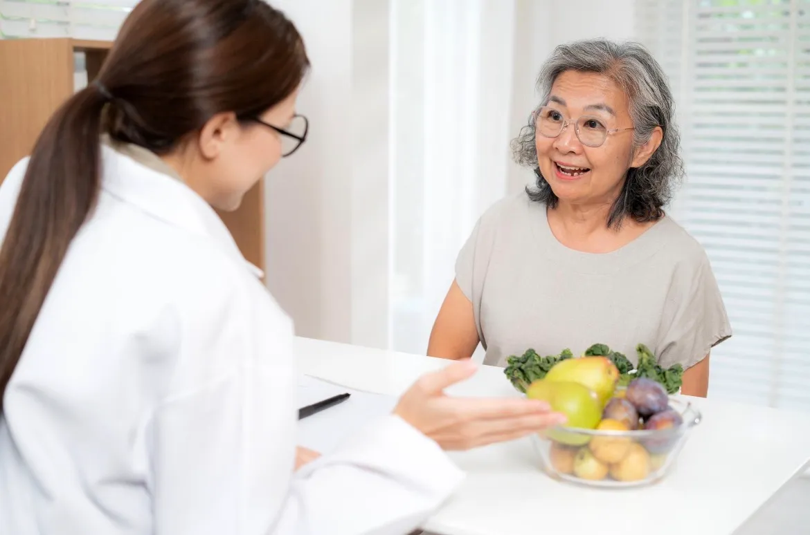 Older woman smiling beside a bowl of fruit during a nutrition consultation