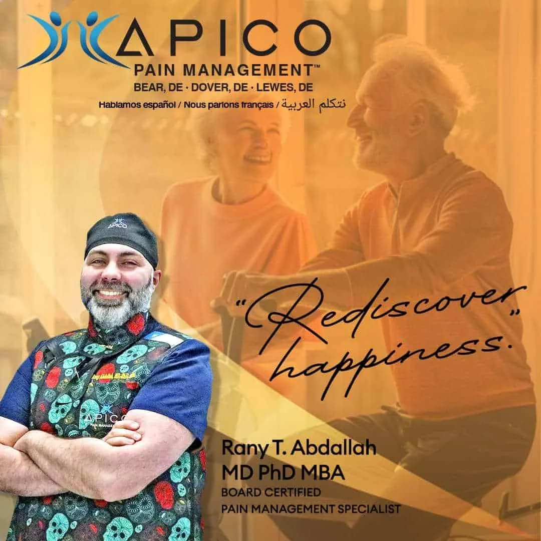 Smiling pain management doctor in colorful medical attire stands confidently with arms crossed, overlaying a warm-toned background showing a happy older couple enjoying a pain-free moment together. Text reads “Rediscover happiness” with branding for APICO Pain Management in Bear, Dover, and Lewes, DE.