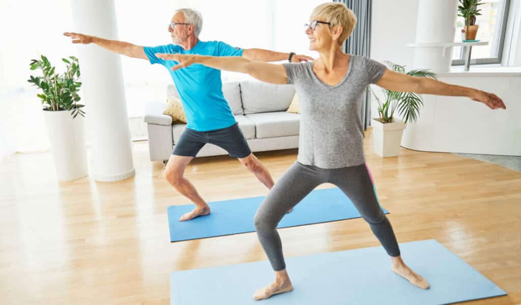 ELDERLY COUPLE PRACTICING YOGA INDOORS ON MAT