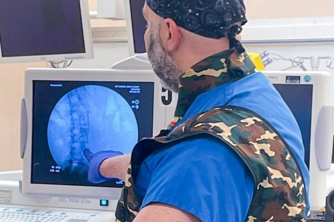 Photo of Dr. Abdallah looking at a monitor displaying a spine.